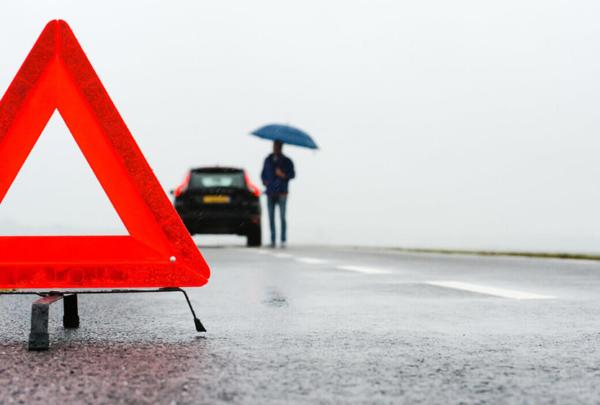 Person standing by broken down car on the side of the road.